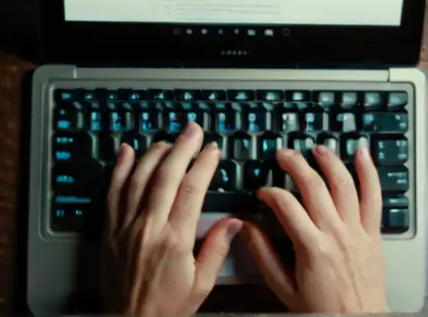 A person's hands typing on a laptop keyboard with fingers curled around