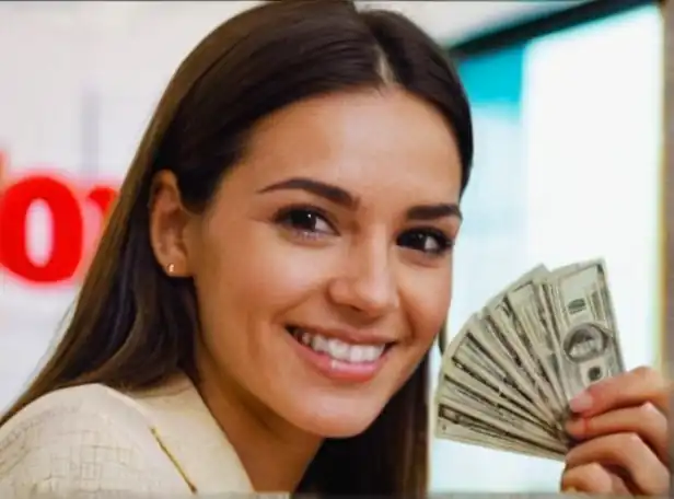 Person holding a credit card and smiling with a stack of cash in the background