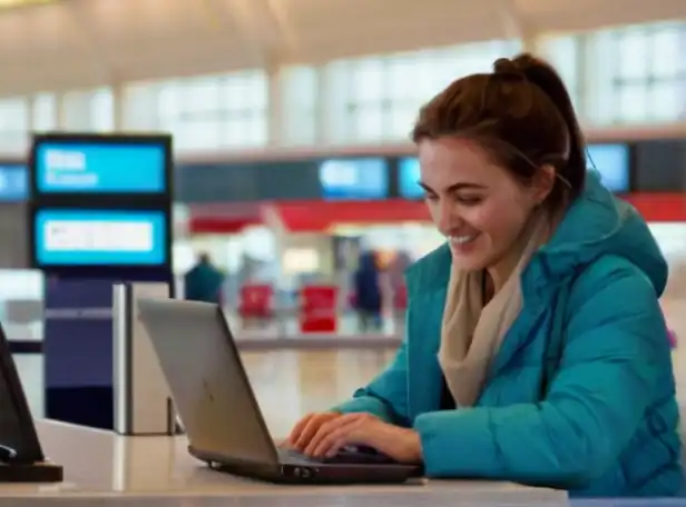 A passenger smiling while checking in on a laptop at airport counter