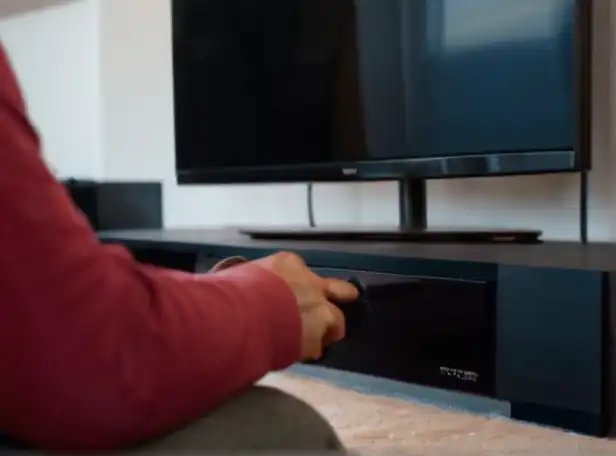 A person sitting in front of a TV console holding a controller