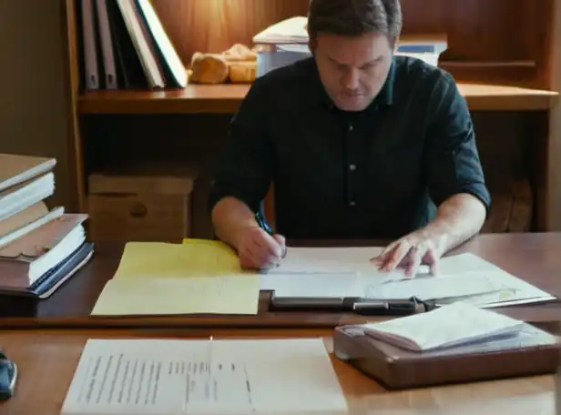 A frustrated person sitting at a desk surrounded by paperwork and pens