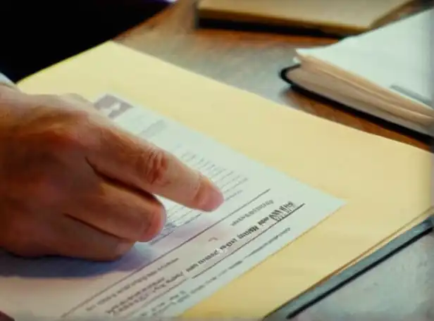 A person signing documents at a table with a property deed