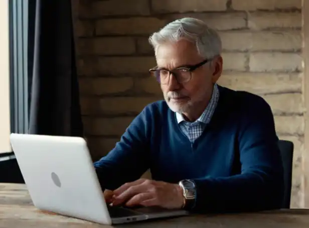 Older adult sitting at a desk with a laptop and phone