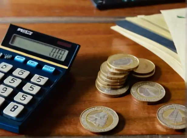 Calculator on desk surrounded by coins and paper