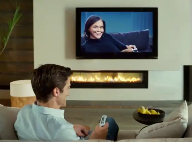 A person smiling on a couch holding a remote control in front of a large screen smart TV