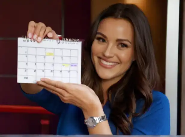 A person smiling while holding a boarding pass and looking at a calendar