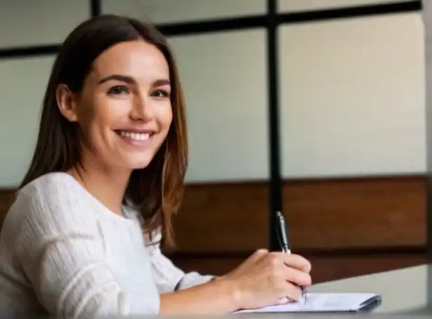 A person holding a pen and smiling while sitting at a desk