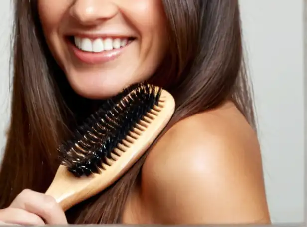 A person smiling holding a hairbrush over a flowing mane