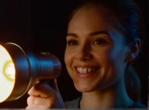 A person in a dark room holding a flashlight and smiling