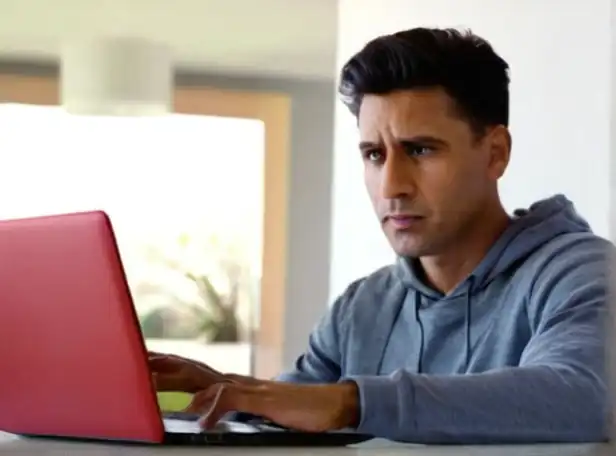 A person sitting in front of a laptop with a concerned expression