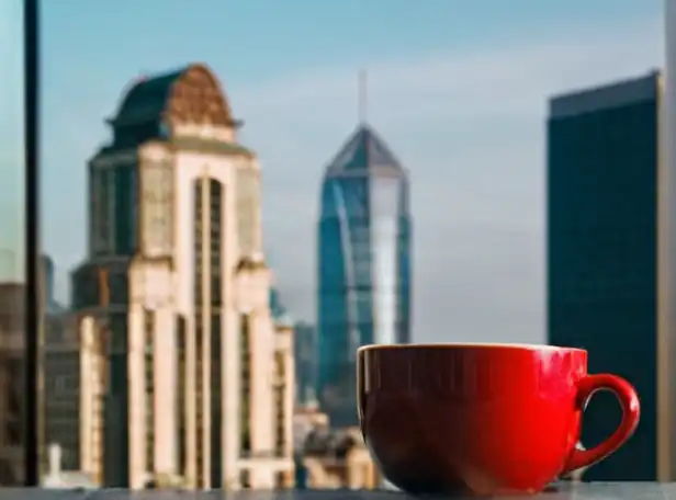 A person holding a cup with coffee and fruits in front of a morning cityscape