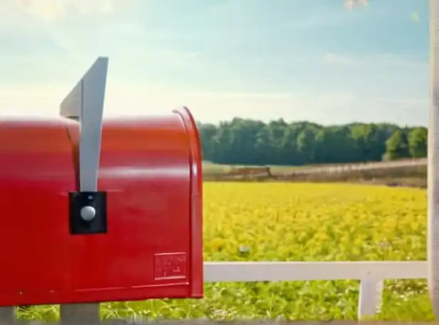 A person holding a mailbox with a stamp or envelope in the foreground and a sunny background